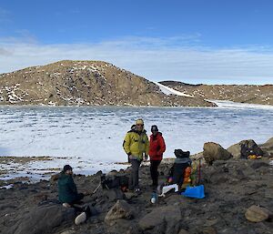 Three people on the rocks with snow in the background