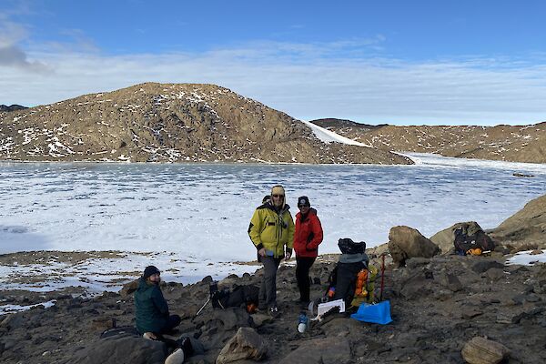Three people on the rocks with snow in the background