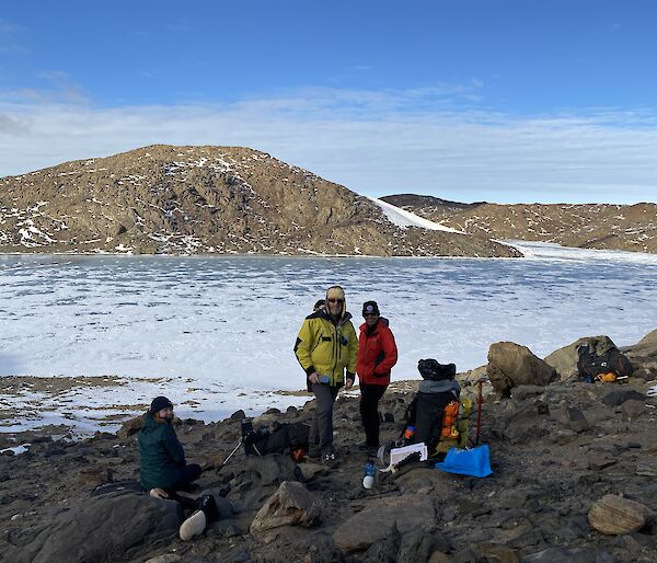 Three people on the rocks with snow in the background