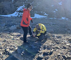 A person tying another person's shoe laces on rocky and snowy ground