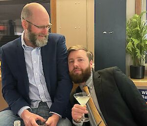 Two bearded smiling men in suit jackets leaning on each other