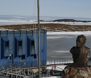 In the foreground the statue of Sir Douglas Mawson and far in the distance two Hägglunds vehicles leave station limits
