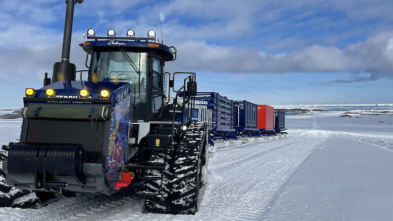 A tractor tows a long train of shipping containers across the ice.