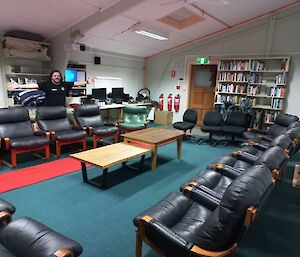 A man stands with arms wide spread in a room with comfy chairs and book cases