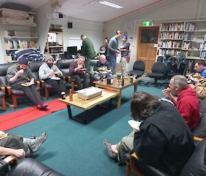 A group of people sit in comfy chairs while eating pizza