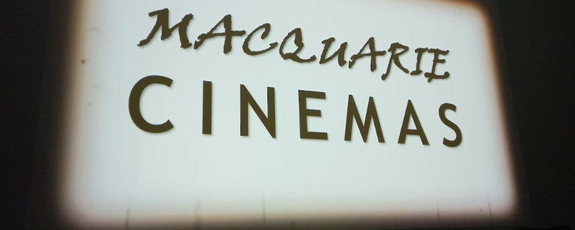 A large white cinema screen with showing a black and white sign saying "Macquarie cinemas"