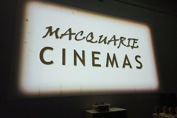 A large white cinema screen with showing a black and white sign saying "Macquarie cinemas"