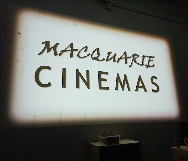 A large white cinema screen with showing a black and white sign saying "Macquarie cinemas"