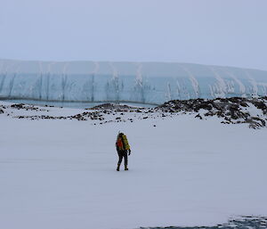 A person walking towards some rocks in the front of a glacier