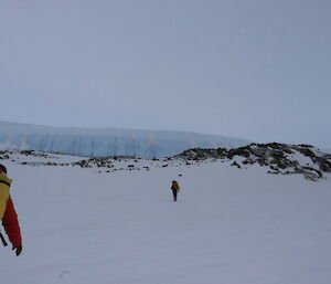 A couple of people walking over snow to a glacier