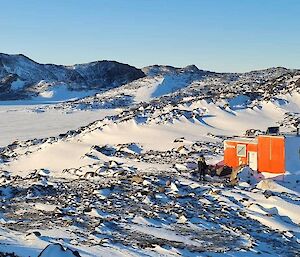 A small hut nestled in snow and hills