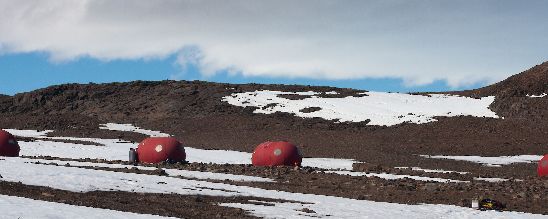 Red portable field huts on brown ice free rock terrain