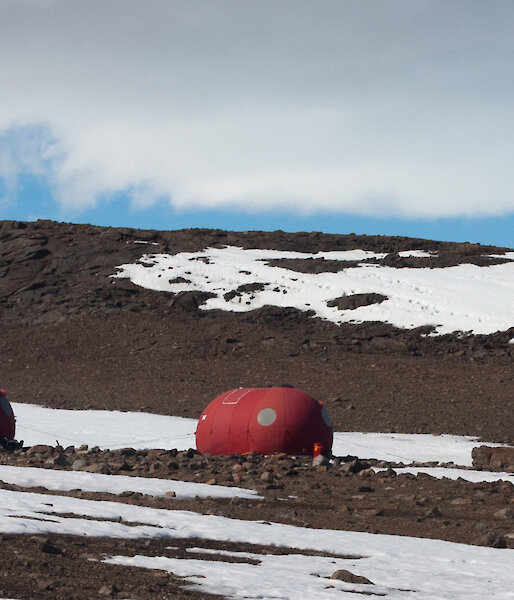 Red portable field huts on brown ice free rock terrain