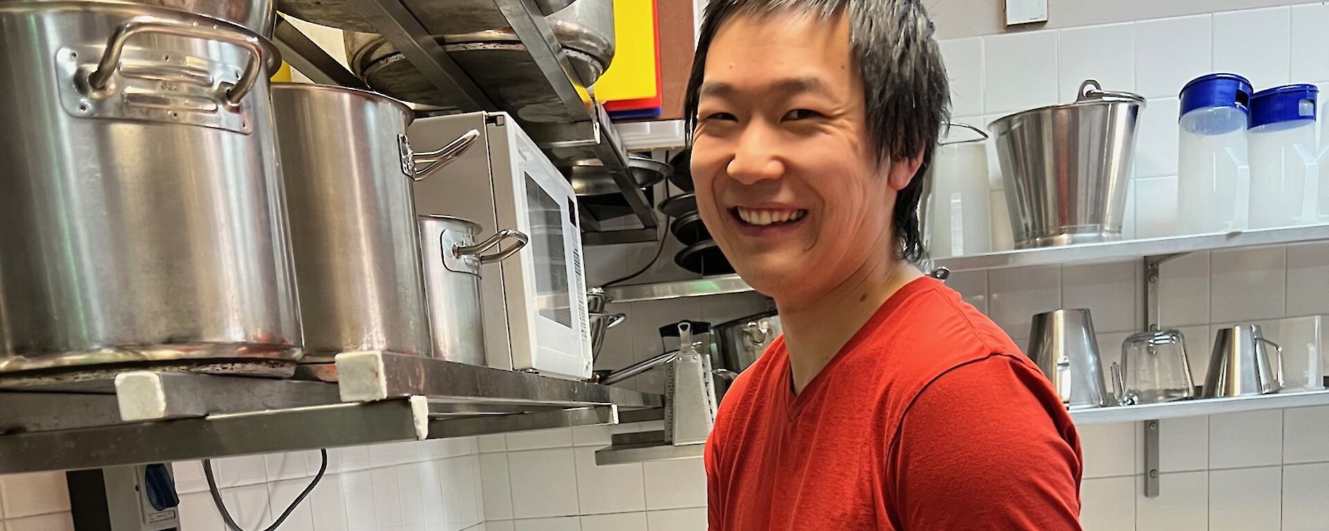 Man in a red t-shirt stands at a kitchen bench making dumplings