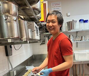 Man in a red t-shirt stands at a kitchen bench making dumplings