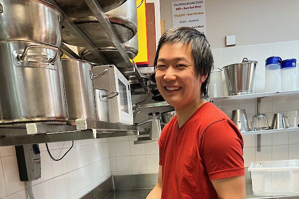 Man in a red t-shirt stands at a kitchen bench making dumplings