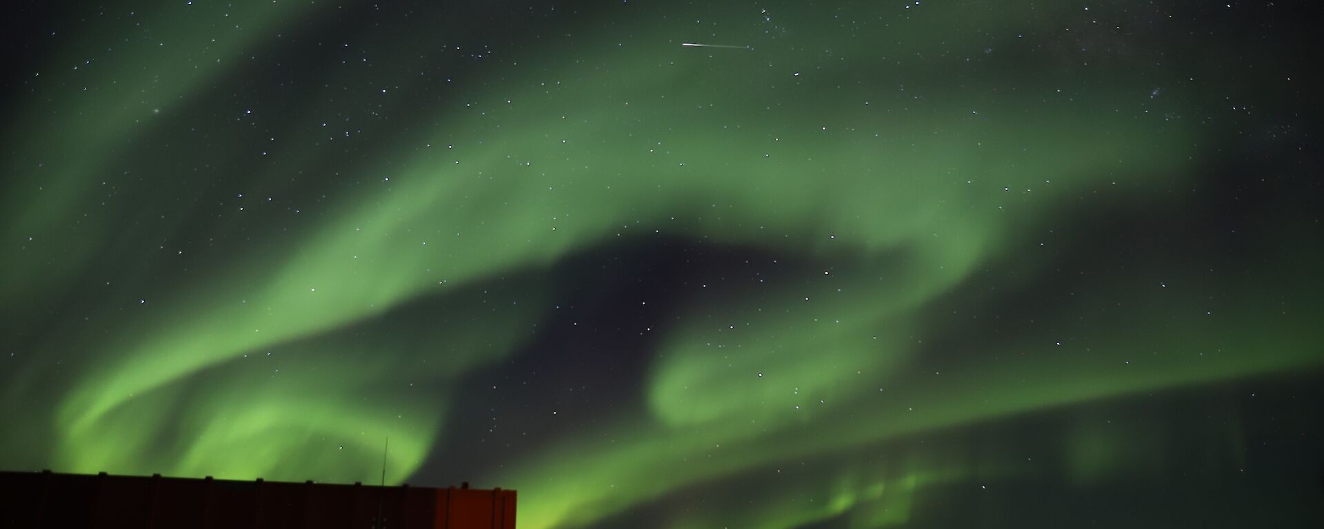 Bright green aurora with shooting stat over station buildings