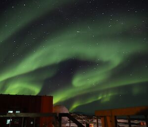 Bright green aurora with shooting stat over station buildings