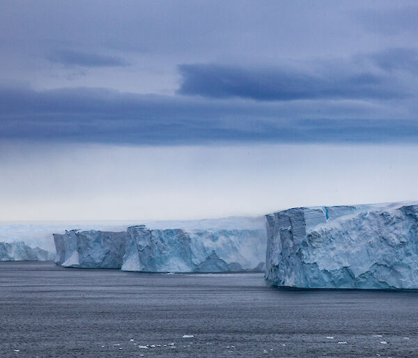 Ice cliffs and ice formations rise out of the water, viewed from a ship.