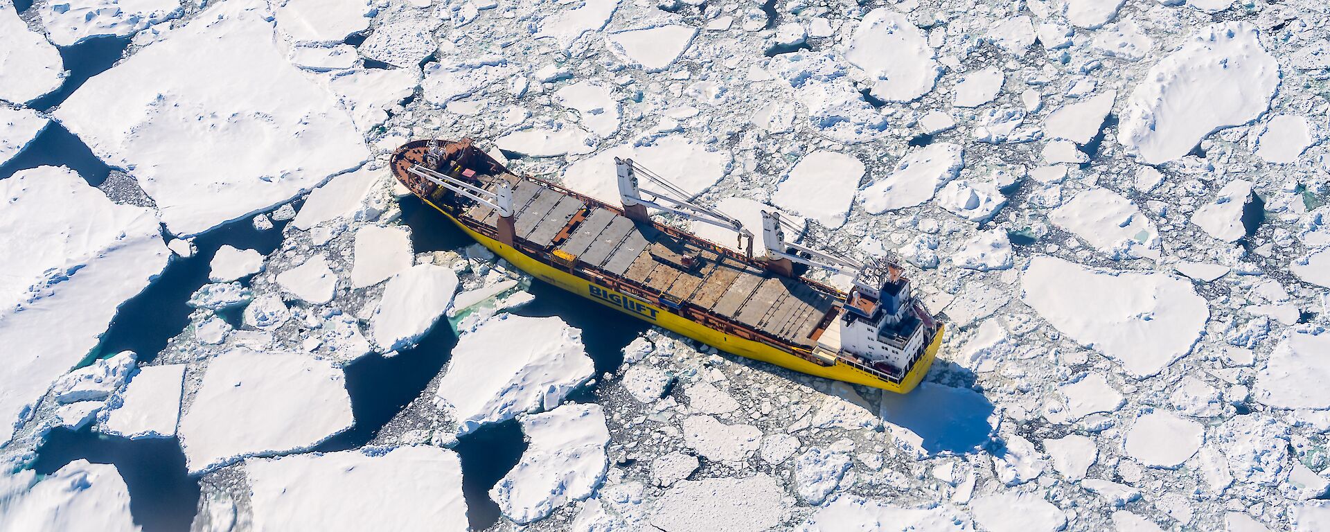 An aerial drone photo of a yellow ship in icy water.