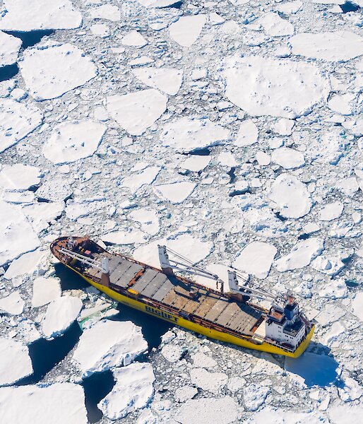 An aerial drone photo of a yellow ship in icy water.