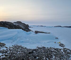 Looking from above on rocky hill down onto field camp below beside ice lake and other rocky islands in distance.