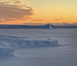 Sunset over sea ice. Clouds in the golden sky reflect fiery and smoky colours above the icescape.