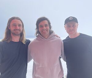 Three young men wearing T-shirts and light hoodie jackets, with arms about each other, posing for a photo outdoors in the snow.