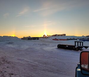 The sun is setting and highlights a tractor parked on the horizon, with other machines and containers in the foreground