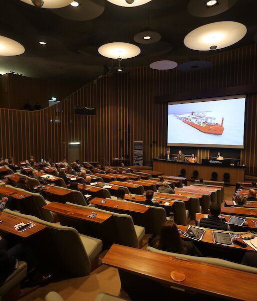 A auditorium filled with people seated. A picture of Australia's icebreaker RSV Nuyina is on the projector screen.