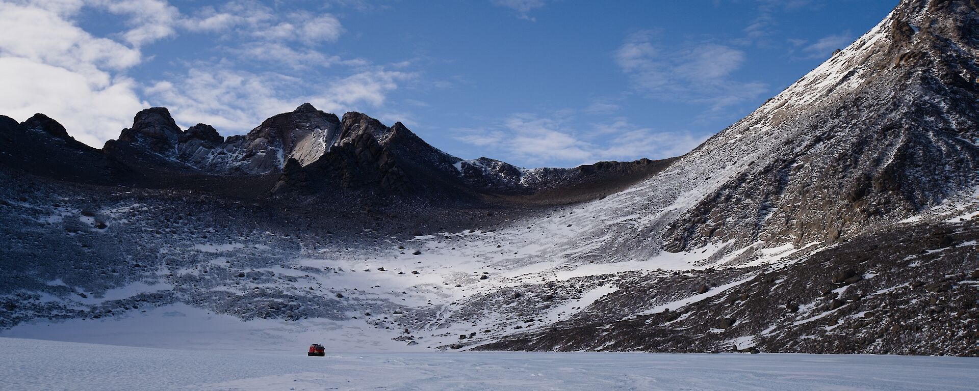 Large frozen lake with Hägglunds in distance, with large mountain peaks rising up above the lake