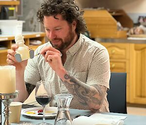 Man sits at table stewn with candles and glasses and paints plastic penguin