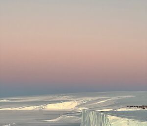 Looking from station across East Bay to the ice cliffs, above a clear sky which is painted pastel lilac and pink by the sunset
