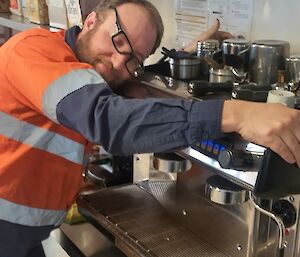 A man with a peaceful expression on his face, leaning against a coffee machine as he enfolds it in a heartfelt hug