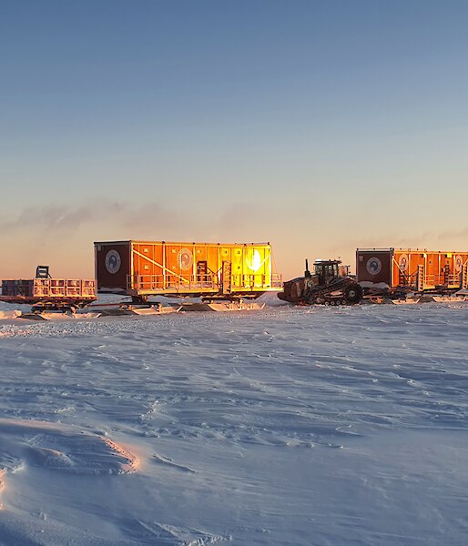 Two tractors tow sleds in golden light