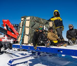 Four people on large sled with pallet behind tractor