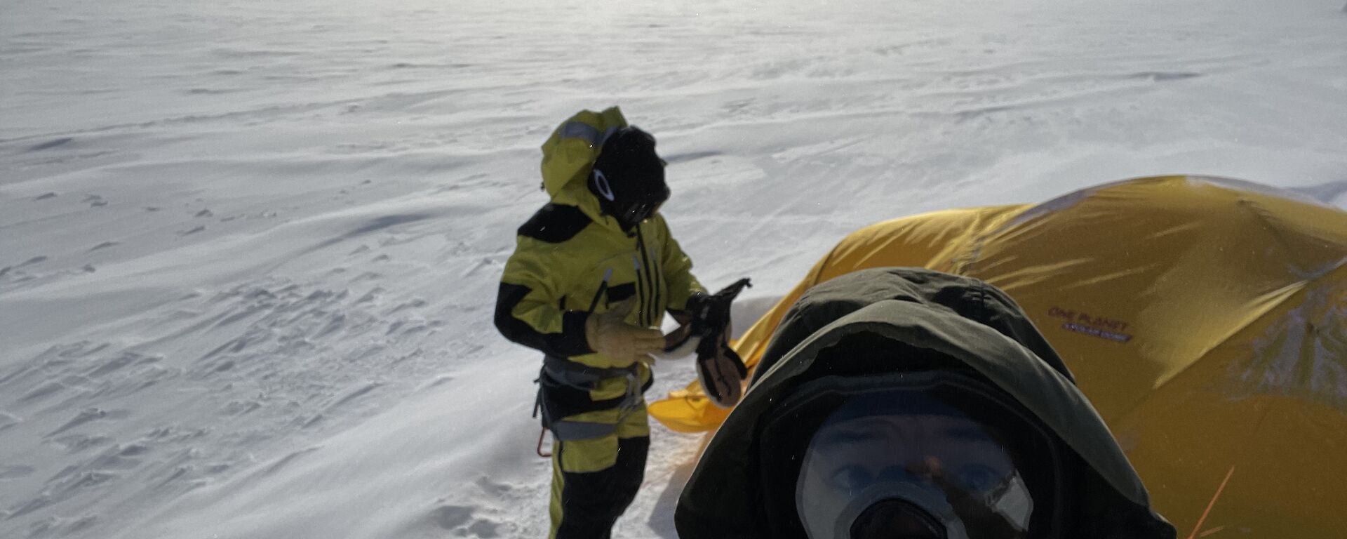 A selfie of two men in outdoor hiking gear with a yellow tent on the snow