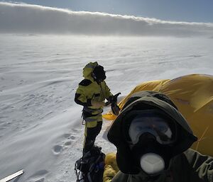 A selfie of two men in outdoor hiking gear with a yellow tent on the snow