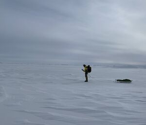 A man dragging a sled across the ice and snow under a grey sky