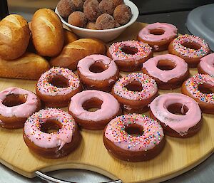 Platter of bread rolls, donuts with pink icing, and donut balls