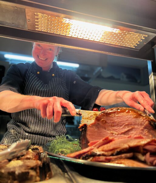 Donna carving a ham leg smiling at camera