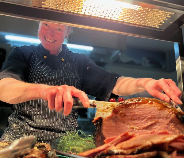 Donna carving a ham leg smiling at camera