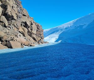 A sunny view of a frozen lake, ice cliff and rocks