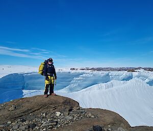 A hiker with a large backpack standing on a rock with ice cliffs in the background