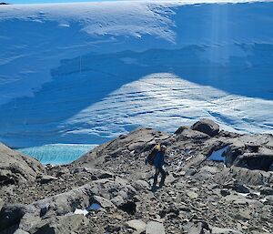 A man walking on rocks with an ice cliff behind him