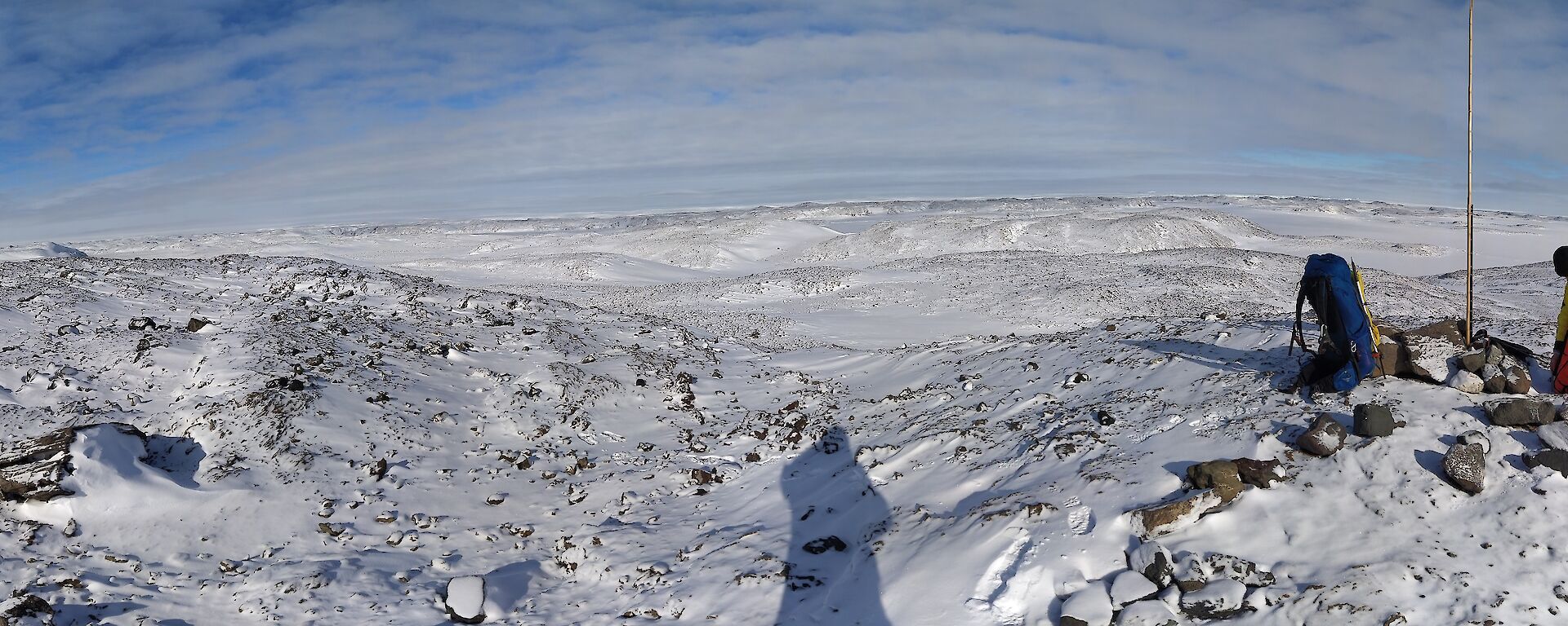 A panoramic shot of the snowy hills with a couple of men looking at a science instrument