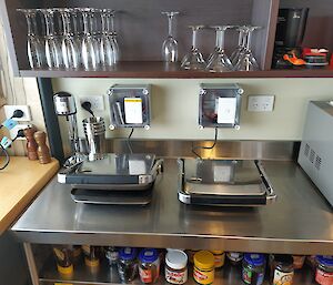 A couple of toasted sandwich makers sit on a metal bench in a tidy kitchen