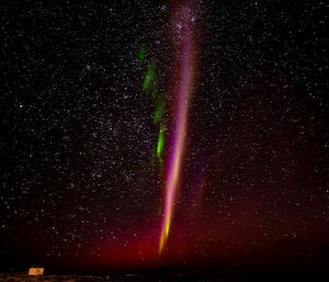 A pinkish vertical streak in the night sky with green lines radiating out from one side.