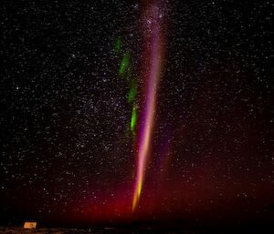 A pinkish vertical streak in the night sky with green lines radiating out from one side