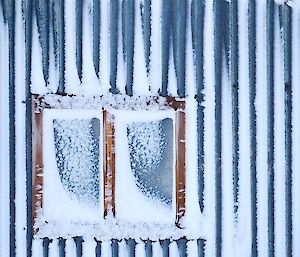 A close up of a window and corrugated outside wall of airplane hangar with snow stuck all over